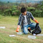 man-wearing-orange-gloves-collecting-garbage-black-bag-min