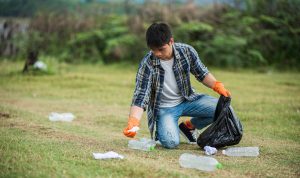 man-wearing-orange-gloves-collecting-garbage-black-bag-min